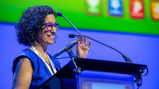 Woman speaking from podium, with a presentation slide in the background
