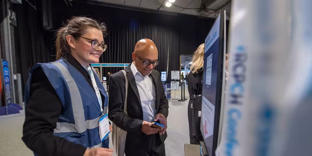 Two people looking at Conference lanyards in the exhibition hall, one wearing a tabard and personalised lanyard